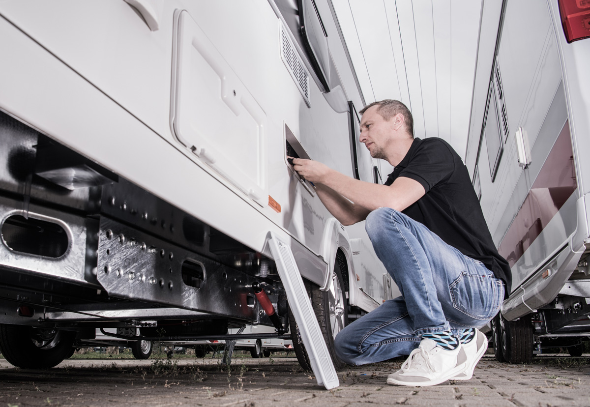 A technician performing a repair on a white RV in El Paso.