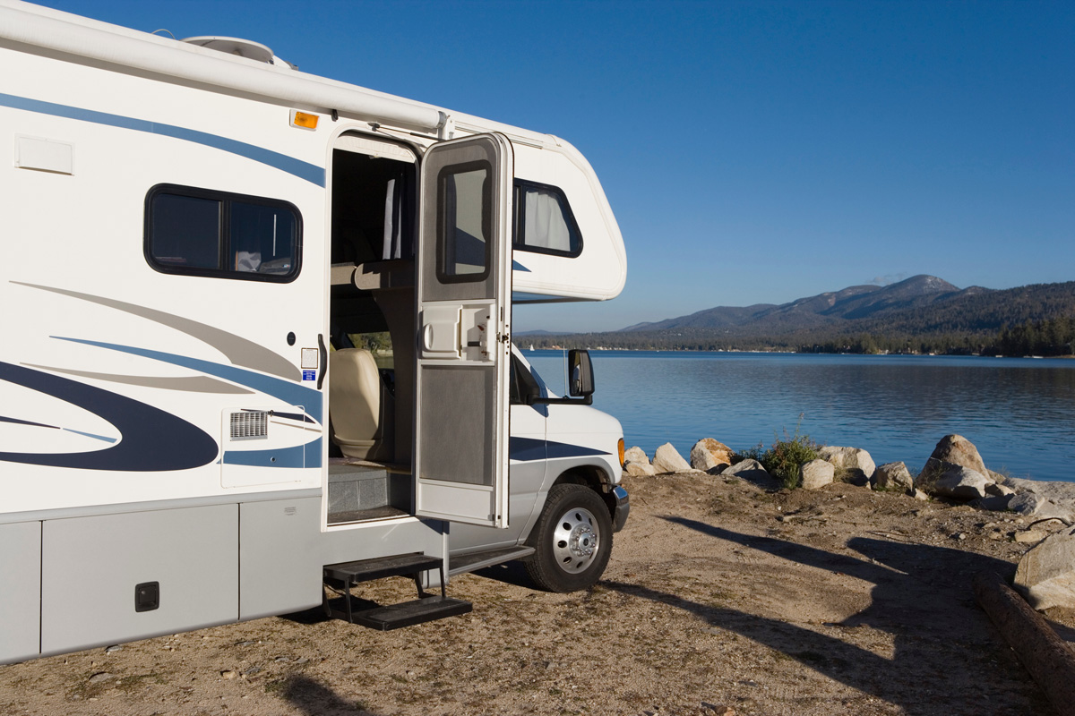 An RV with a door open in front of a lake in El Paso.
